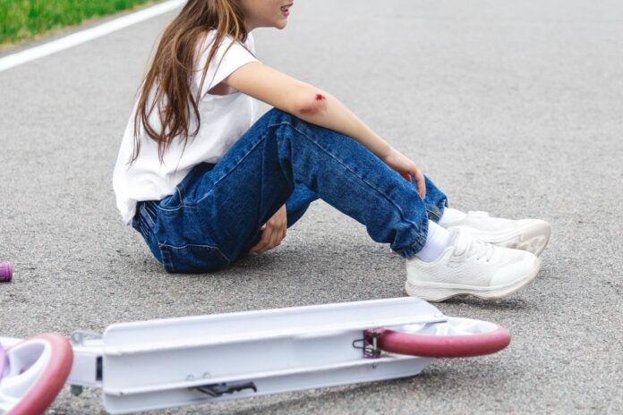 An image of a young girl with blood on her arm and a scooter on the ground nearby.