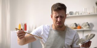 Young man tasting cooked food with disgusted face expression