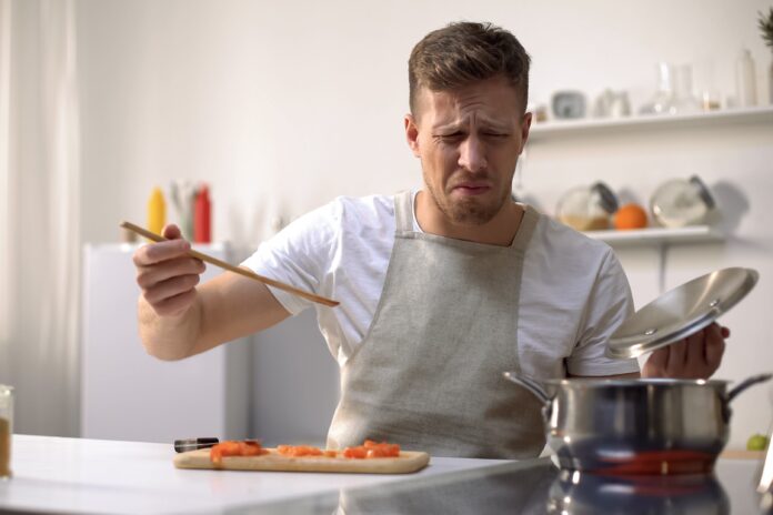 Young man tasting cooked food with disgusted face expression