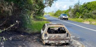 A burnt-out car parked beside a road.