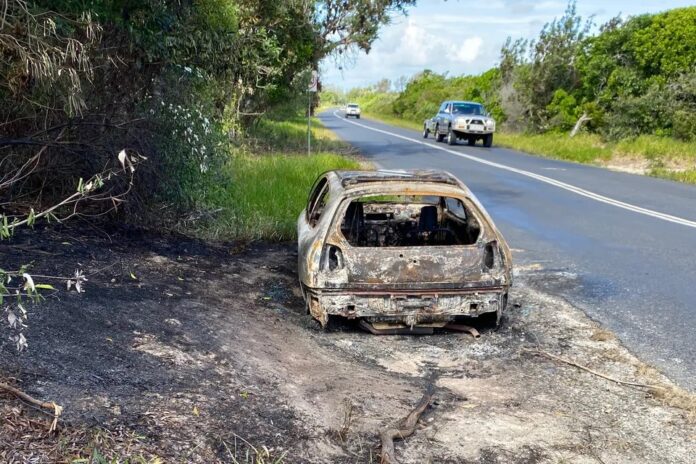 A burnt-out car parked beside a road.
