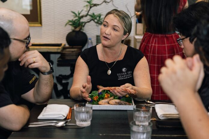 Silver Seas Seafood managing director Jacky Cartwright speaks at a table, while eating fresh seafood.