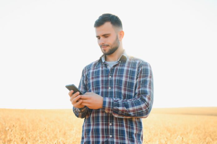 A farmer in an agricultural field holding a phone.