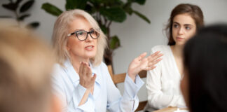 A businesswoman talks to colleagues at a meeting around a table. Picture by Shutterstock.