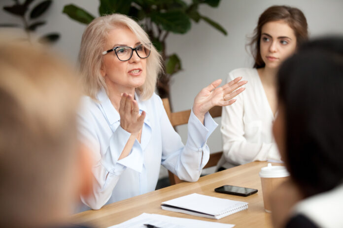 A businesswoman talks to colleagues at a meeting around a table. Picture by Shutterstock.