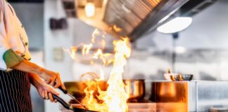 A cook with flames from a frypan in a restaurant kitchen. Picture: Shutterstock.