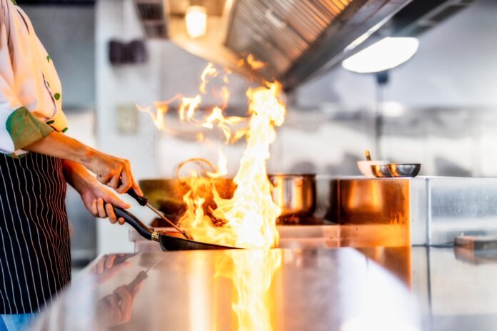 A cook with flames from a frypan in a restaurant kitchen. Picture: Shutterstock.