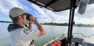 A ranger looking through binoculars from a boat.
