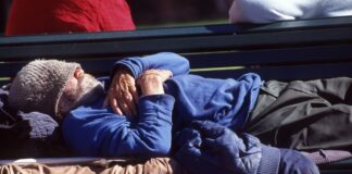 A homeless man sleeping on a park bench.