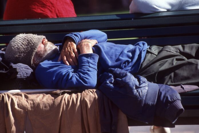A homeless man sleeping on a park bench.