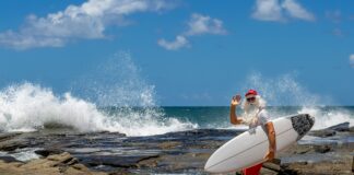 A man in Christmas clothes with a surfboard at the beach. Picture: Shutterstock.