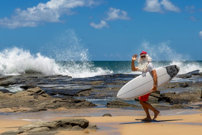 A man in Christmas clothes with a surfboard at the beach. Picture: Shutterstock.