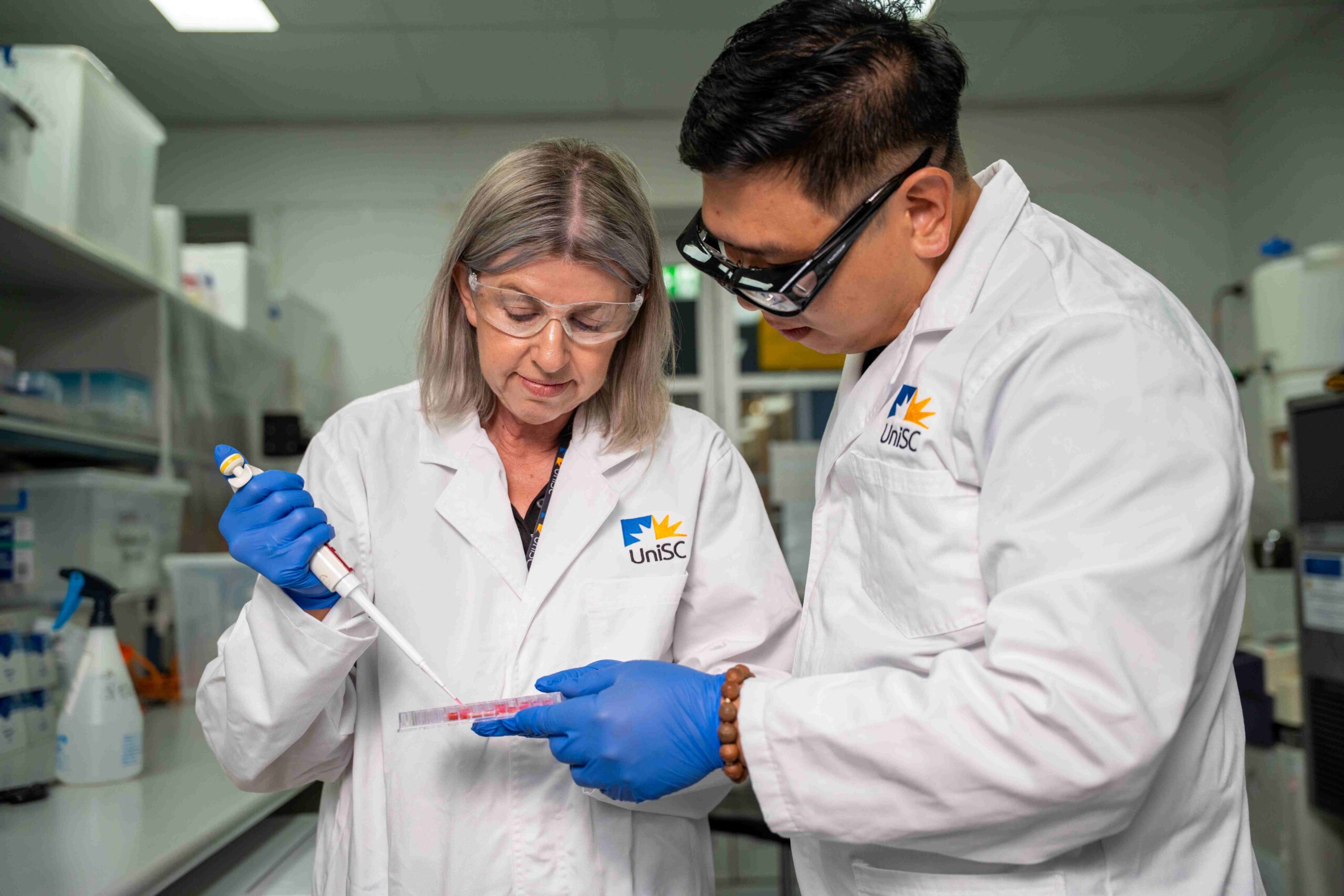 PhD student Lisa Randall and supervisor Dr Trong Tran inject compound into human cells grown in culture plates.