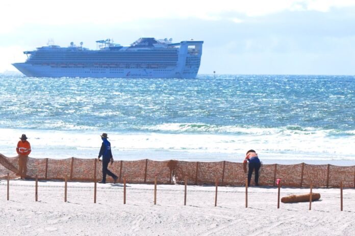 A fence being installed along Bribie Island, with a ship in the background.