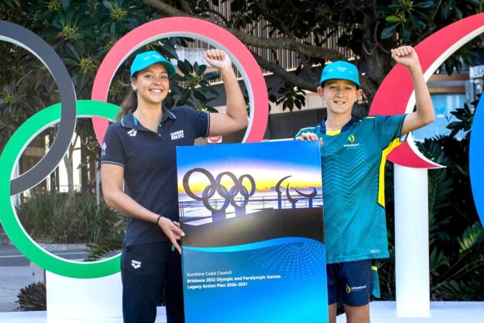 Young local athletes Rylee Smith and Rylan Wooster in front of Olympic rings, holding a legacy plan for the Sunshine Coast.