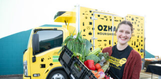 An OzHarvest rep with food in front of a delivery truck.