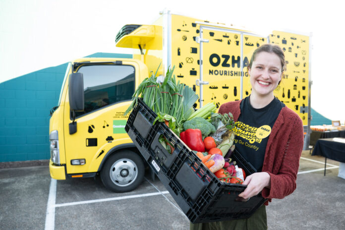 An OzHarvest rep with food in front of a delivery truck.