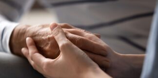Shutterstock image of young woman holding old person's hand.