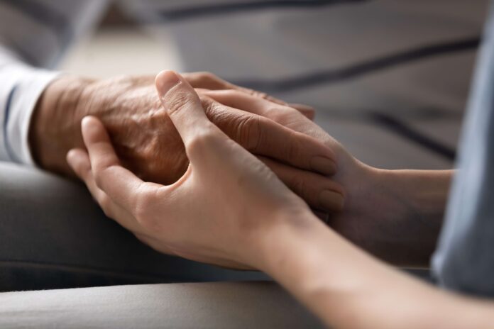 Shutterstock image of young woman holding old person's hand.
