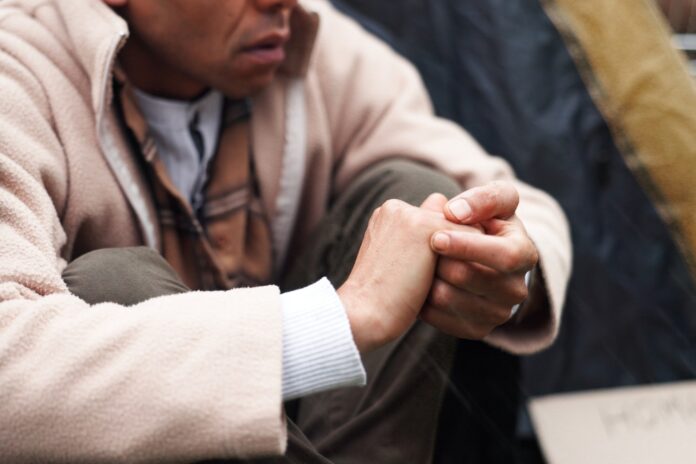A homeless person sitting with hands clasped.