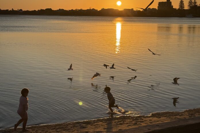 Kids playing at the water's edge Bulcock Beach at sunset