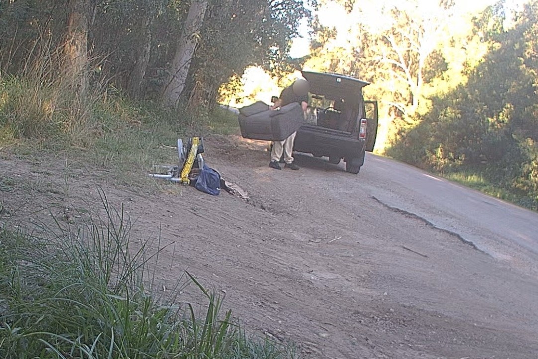 A person dumping a lounge chair and other items beside a road.