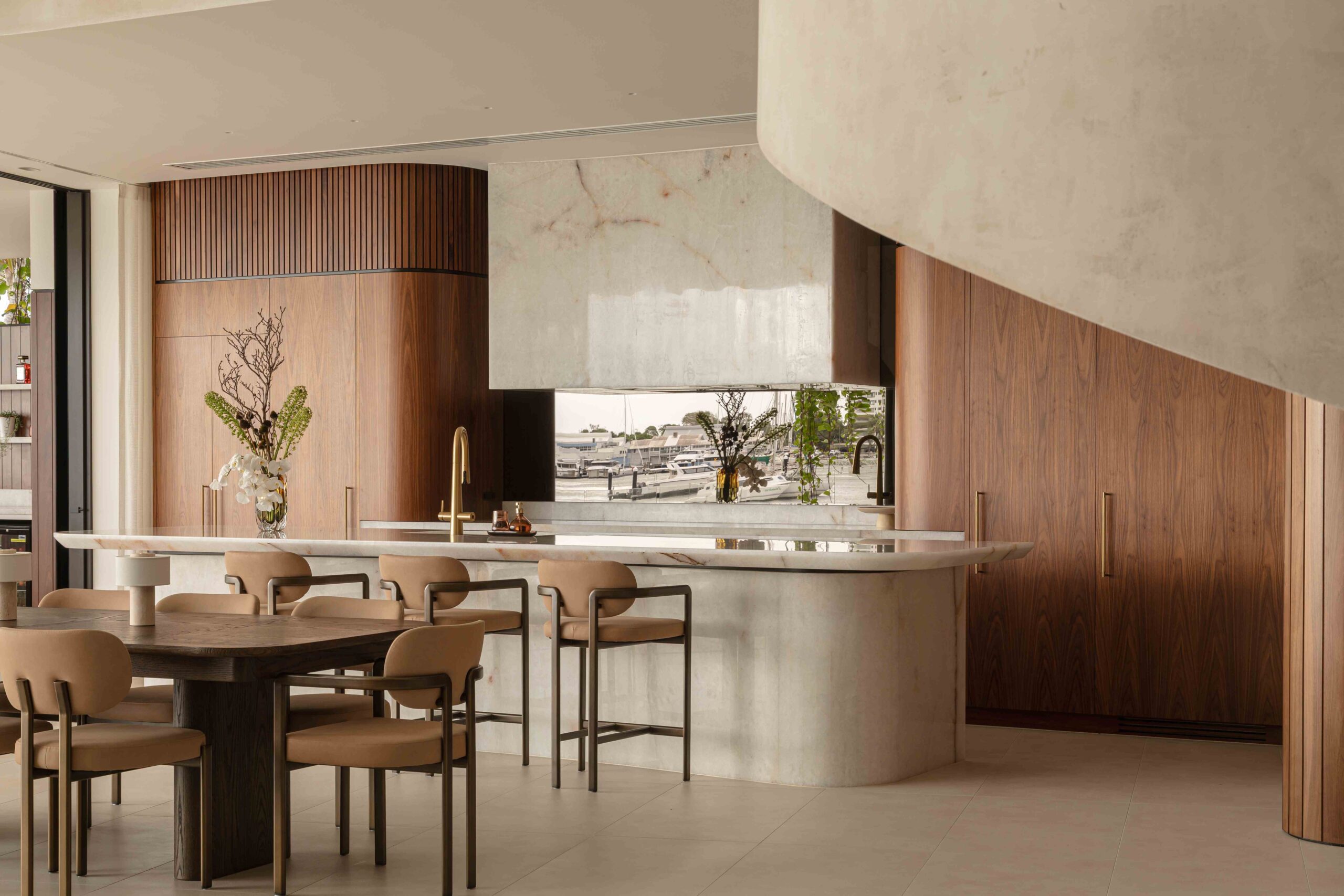 A modern, architectural timber and stone kitchen including a timber dining table and curved concrete element.