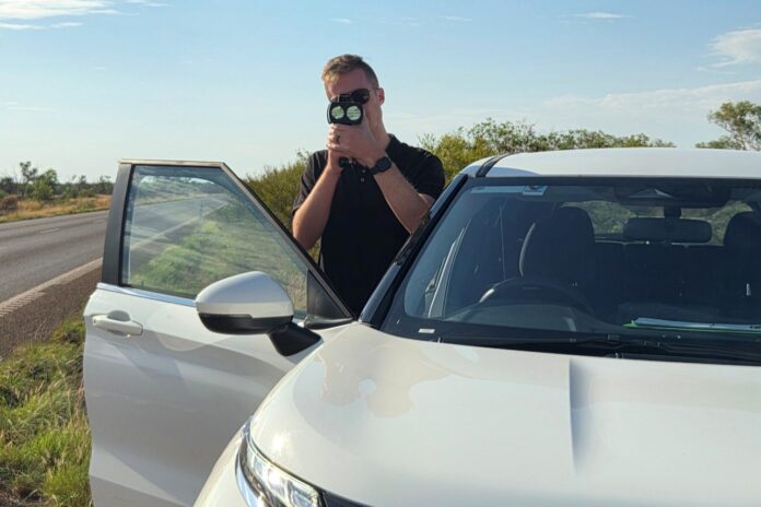 Dr Levi Anderson with a laser speed measurement device by the road.