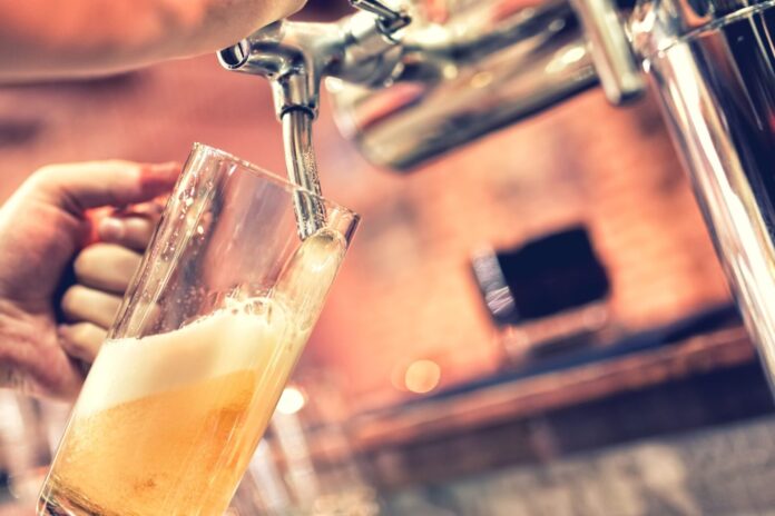 A hand is holding a beer glass and filling it with tap beer