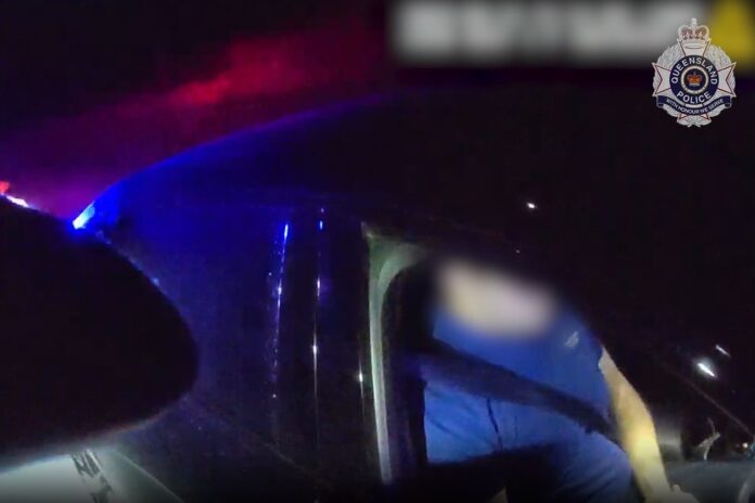 A motorist in driver's seat being talked to by police at night.
