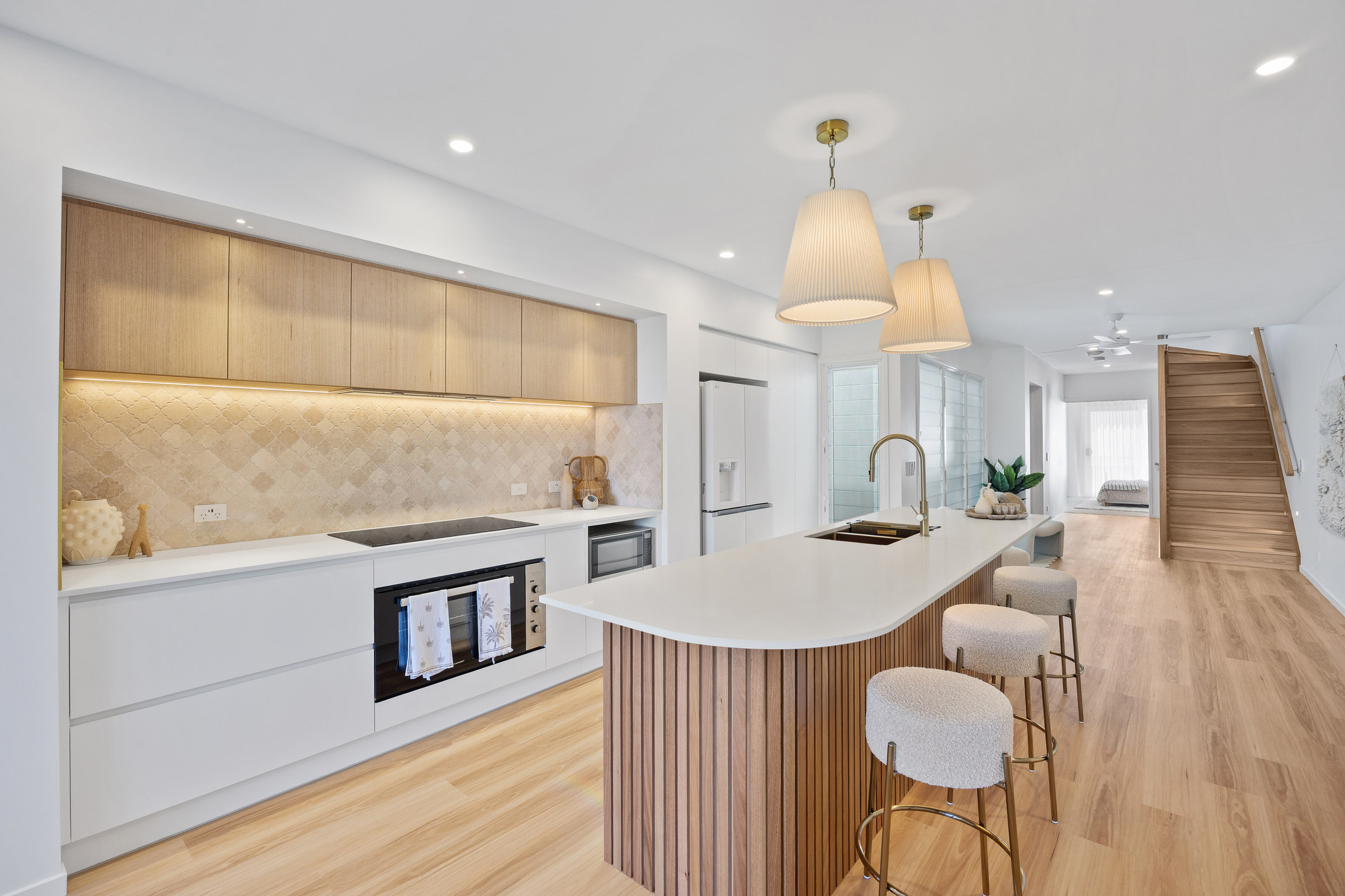 A modern kitchen featuring white cabinets, timber island and timber flooring.