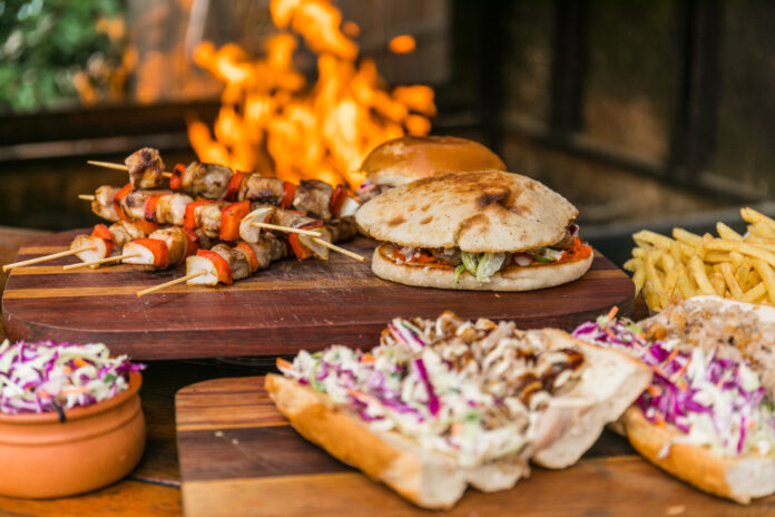 Burgers, rolls and kebabs on sticks in front of a fireplace.