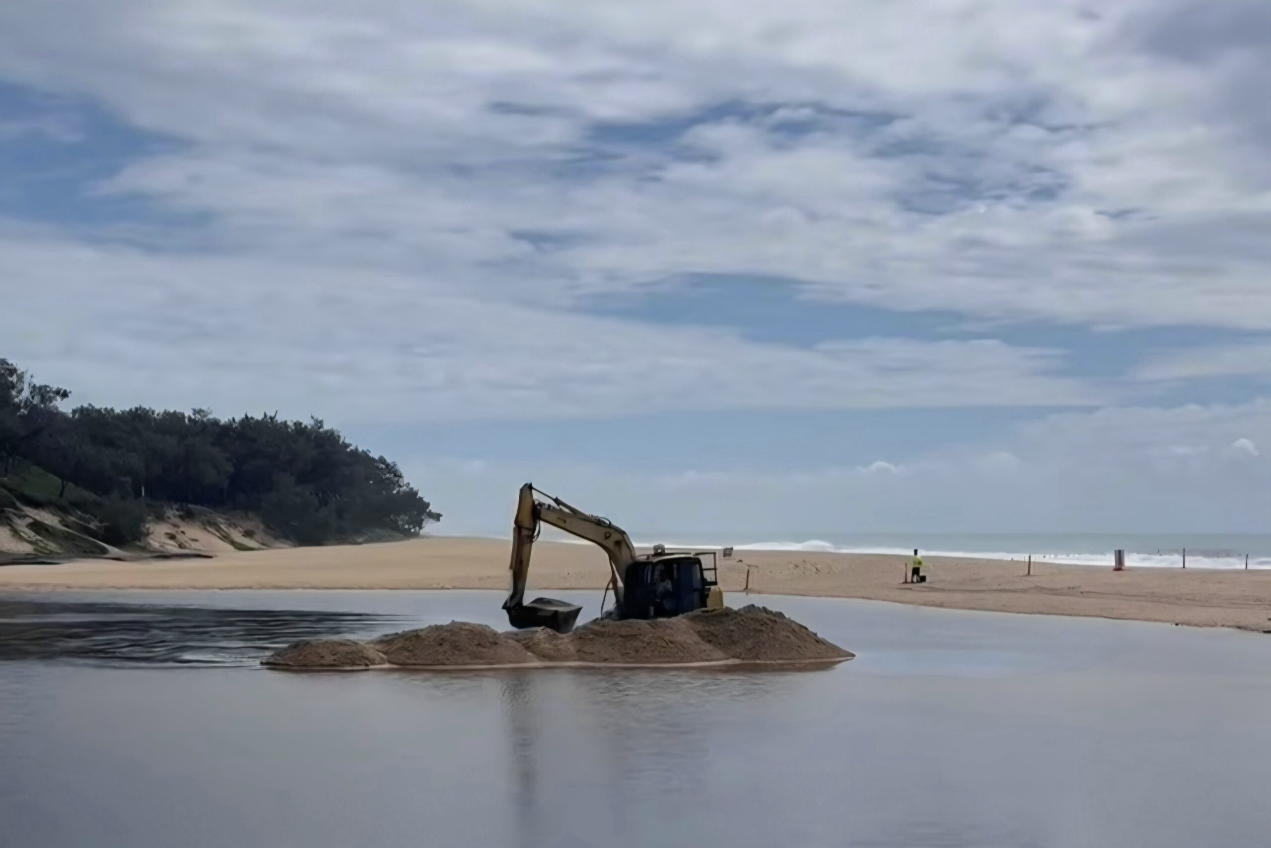 A digger moves sand on a beach.