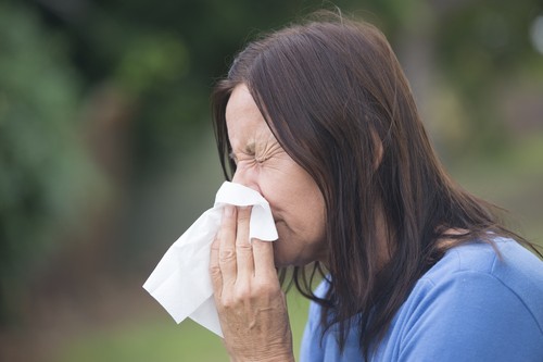 Woman sneezing into a tissue